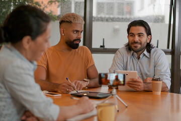 Professional latin group of entrepreneurs with tablet talking online to business team at meeting inside coworking office. Unity, teamwork, collaboration concept..