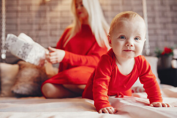 Fototapeta premium Beautiful mother in a red dress. Family with cristmas gifts. Little boy on a bed