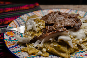 Mexican green chilaquiles with cecina beef steak on wooden background