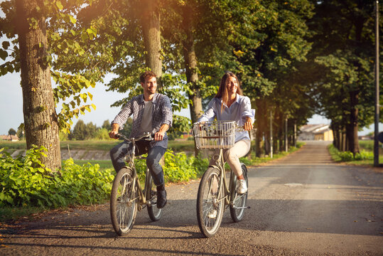 Authentic shot of young carefree happy couple in love is having fun and enjoying time together while riding bicycles in a green park in a sunny day.