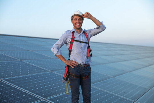Maintenance assistance technical worker in uniform is smiling satisfied of his work after checking operation and efficiency performance of photovoltaic solar panels on roof at sunset.