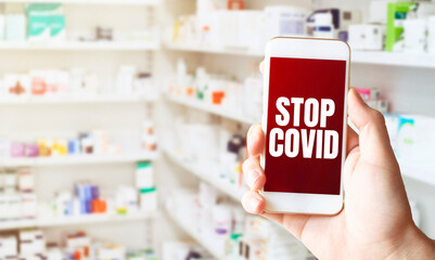 hand holding smart phone in pharmacy drugstore. Text STOP COVID