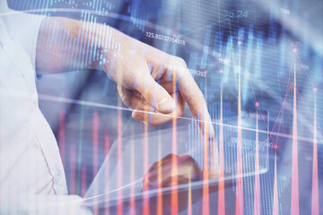 Double exposure of man's hands holding and using a digital device and forex graph drawing. Financial market concept.