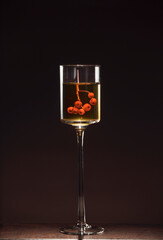 Tall glass on a thin stem with a bunch of red rowan in wine