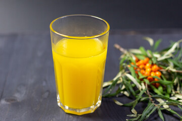 glass of fresh sea buckthorn juice on black background and fresh berries