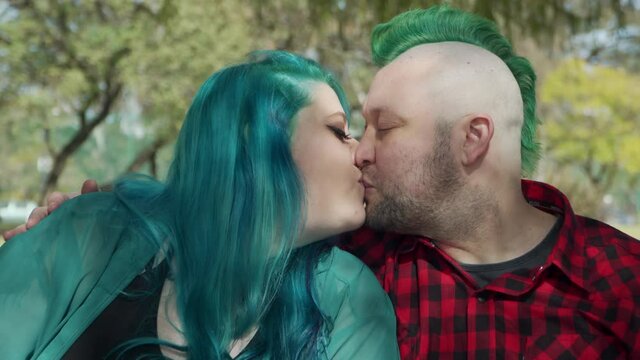 Dolly in shot of a couple of alternative people sitting on a bench and kissing 