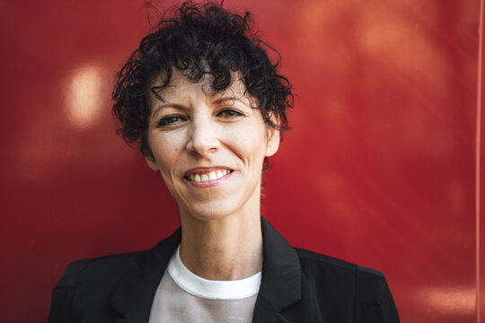 Close Up Portrait Of Confident Mature Business Woman In Suit Against Red Wall