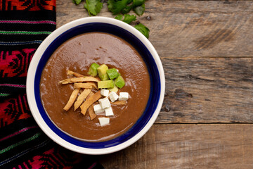 Mexican cream of bean soup with avocado and cheese on wooden background
