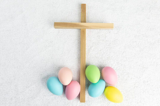 Colorful Easter eggs and a wooden cross show the religious and secular side of Easter on a white terry cloth background