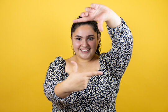 Young Beautiful Woman With Curly Hair Over Isolated Yellow Background Smiling Making Frame With Hands And Fingers With Happy Face