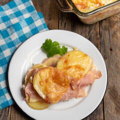 Scalloped potatoes with ham and cheese on wooden background