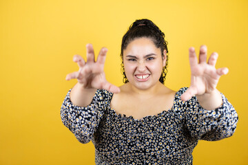Young beautiful woman with curly hair over isolated yellow background smiling funny doing claw gesture as cat, aggressive and sexy expression
