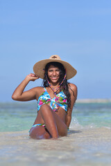 Hispanic Woman siting on beach inside blue water splash. Natural laughing holding straw hat , Beach Background