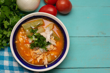 Mexican chicken soup with vegetables and rice on turquoise background
