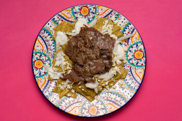 Mexican green chilaquiles with cecina beef steak on pink background