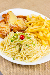Spaghetti with slices of chive and spice. Chicken with cheese and french fries. Selective focus