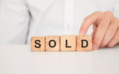 Close up young man's hand in white shirt wooden block cube for Sold wording on white marble table floor