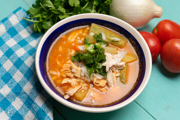 Mexican chicken soup with vegetables and rice on turquoise background