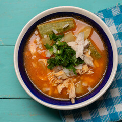 Mexican chicken soup with vegetables and rice on turquoise background