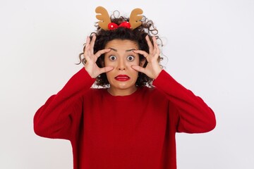 Young arab woman with curly hair wearing christmas headband on white background, keeping eyes opened to find a success opportunity.