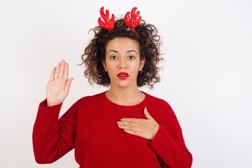Young arab woman with curly hair wearing christmas headband standing on white background Swearing...