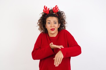 Young arab woman with curly hair wearing christmas headband standing on white background In hurry pointing to watch time, impatience, upset and angry for deadline delay.