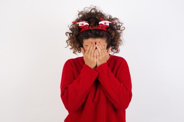 Young arab woman with curly hair wearing christmas headband standing on white background covering her face with her hands, being devastated and crying. Sad concept