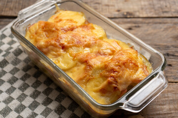 Scalloped potatoes with ham and cheese on wooden background
