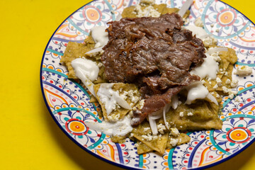 Mexican green chilaquiles with cecina beef steak on yellow background