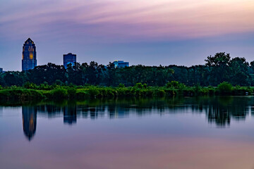 Naklejka premium Des Moines skyline reflecting in a lake at sunrise.