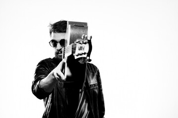 A man plays the guitar in a black leather jacket with sunglasses on a light background