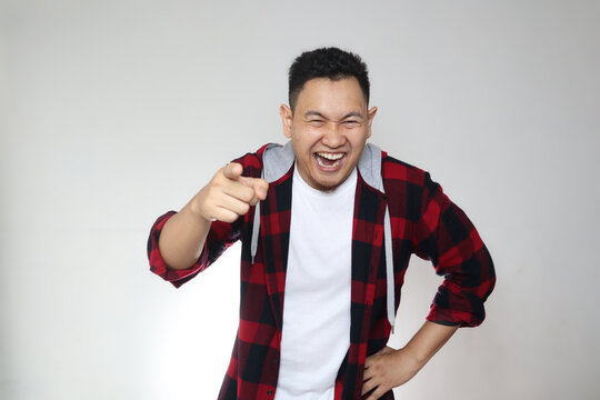 Portrait of funny Asian man laughing hard and pointing forward, bully expression