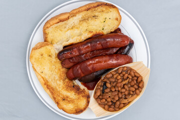 Overhead view of BBQ meal of links, baked beans, and butter toasted bread will taste as delicious as it looks.