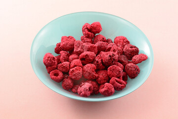 Freeze dried red raspberries in blue bowl on pink background