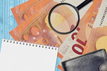 10 euro bills and magnifying glass with black purse and notepad. Concept of counterfeit money....
