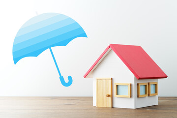 Home insurance. Miniature house and illustration of umbrella. Wood table and white background.