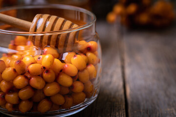 Healthy autumn dessert based on freshly harvested sea buckthorn ripe berries in jar with fresh liquid honey. Selective focus. Shallow depth of field.