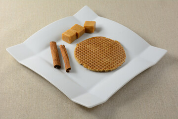 Caramel cinnamon waffle cookie snack with caramel candies and cinnamon sticks on white snack dish on light brown tablecloth