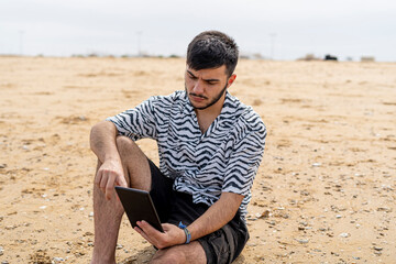 Adolescente leyendo un libro electrónico sentado en la arena 