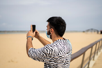 Hombre Joven con mascarilla en paseo de marítimo haciendo fotos al mar 