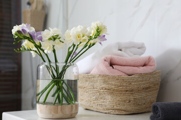 Fototapeta na wymiar Beautiful freesia flowers and basket of towels on countertop in bathroom
