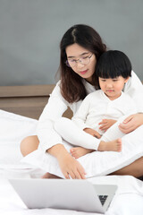 Mother hugging her daughter using laptop in bed