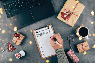 Fototapeta na wymiar Christmas online shopping flat lay. Girl writing shopping list. Laptop, present box, cup of coffee