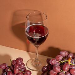 The wineglass with red wine and two bunches of fresh red grapes isolated on beige background. Wine with shadow on the wall.