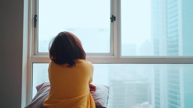 Asian woman sitting and looking outside after being locked down. Feeling lonely and homesick, concept stay home
