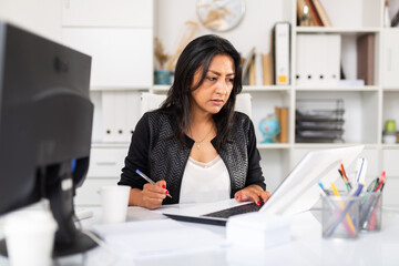 Focused hispanic business woman working alone on laptop in modern office ..