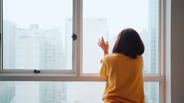 Asian woman looking outside after being locked down. Feeling lonely and homesick, concept stay home
