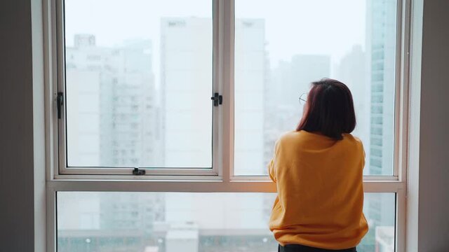 Asian woman looking outside after being locked down. Feeling lonely and homesick, concept stay home
