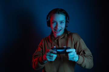 Attractive girl playing online video games and using headphones and joystick. The gambling face of gamer girl. Blue neon background. Gamer concept. - obrazy, fototapety, plakaty