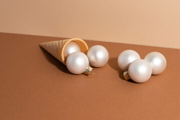 The ice-cream's waffle cone with white christmas balls isolated on beige background. Christmas concept. Horizontal photo. Flat lay. Idea for decoration.